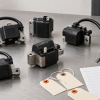 Generic aftermarket ignition coil modules beside a caliper and blank fitment review worksheet on a clean workbench